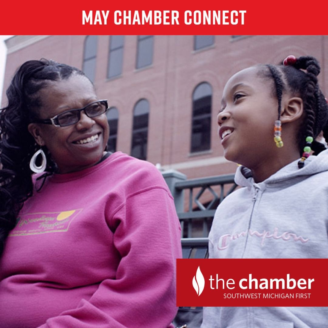 A smiling African American woman in a bright pink sweatshirt looks at a young African American girl with braids in a gray zip up hoodie who is also smiling
