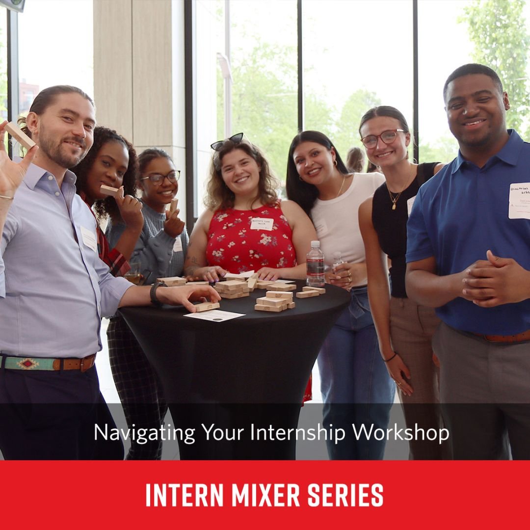 seven male and female interns gather around a tall cocktail table playing Jenga at an intern mixer event in The Catalyst Center