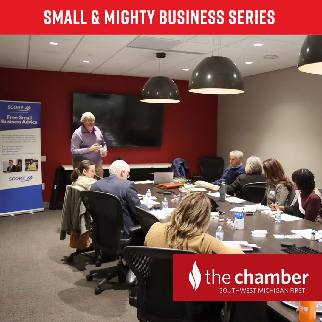 Small & Mighty business event - small group of business professionals who are seated in a conference room listening to a presenter and taking notes